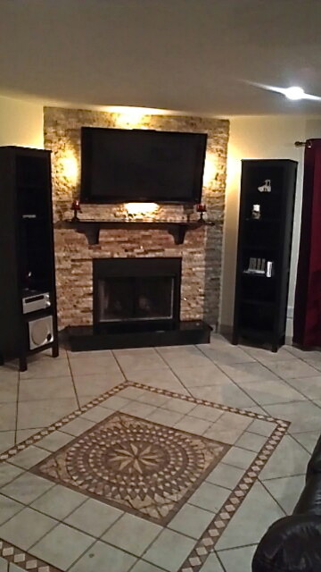 Cette photo montre un grand salon tendance avec un mur beige, un sol en carrelage de céramique, une cheminée standard, un manteau de cheminée en pierre et un téléviseur fixé au mur.