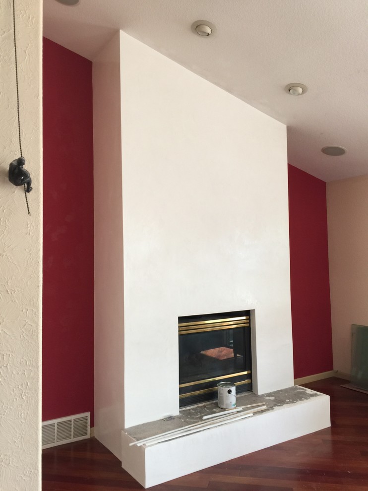 Cette image montre un salon minimaliste avec un mur blanc et un manteau de cheminée en plâtre.