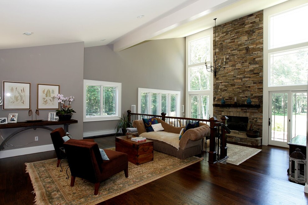 На фото: большая открытая гостиная комната в стиле неоклассика (современная классика) с серыми стенами, темным паркетным полом, стандартным камином, фасадом камина из камня и коричневым полом