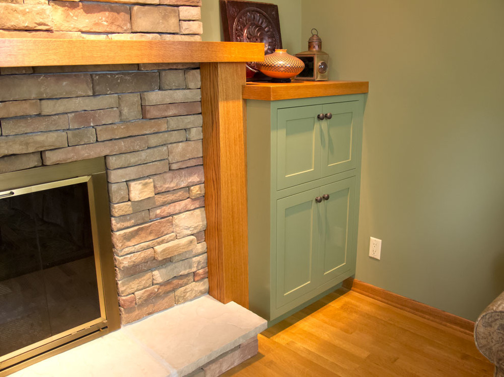 Mid-sized enclosed medium tone wood floor living room library photo in Minneapolis with green walls, a standard fireplace, a stone fireplace and a tv stand