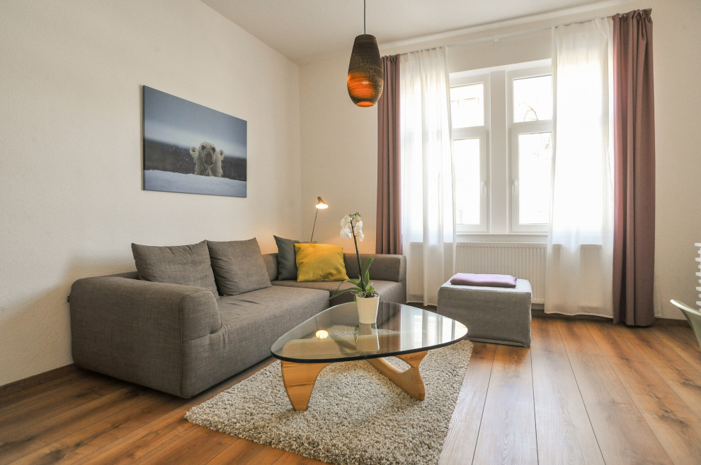 На фото: гостиная комната среднего размера в скандинавском стиле с белыми стенами, полом из ламината и телевизором на стене с