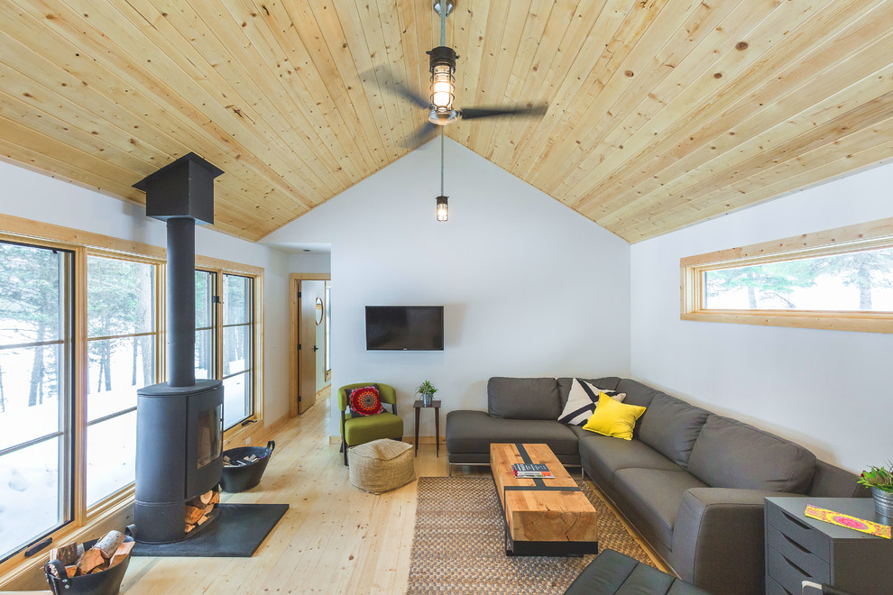 Ejemplo de salón rural con paredes blancas, suelo de madera clara, estufa de leña, televisor colgado en la pared y suelo beige