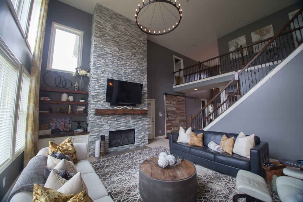 На фото: огромная открытая гостиная комната в стиле неоклассика (современная классика) с серыми стенами, ковровым покрытием, стандартным камином, фасадом камина из камня и телевизором на стене с