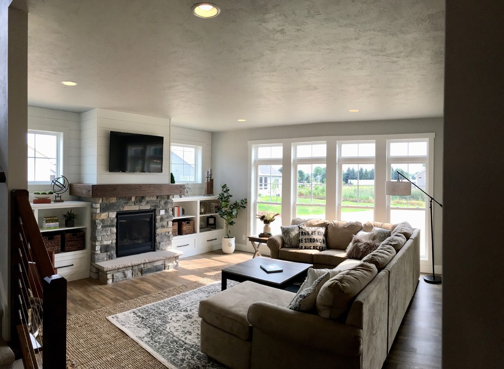 Cette photo montre un grand salon nature ouvert avec un bar de salon, un mur gris, un sol en vinyl, une cheminée standard, un manteau de cheminée en pierre, un téléviseur encastré et un sol marron.