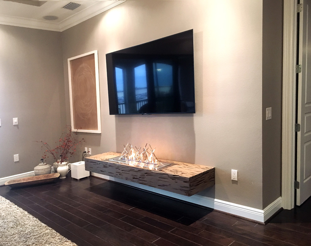 Foto de salón abierto moderno de tamaño medio con paredes grises, suelo de madera en tonos medios, chimenea lineal, marco de chimenea de madera y televisor colgado en la pared