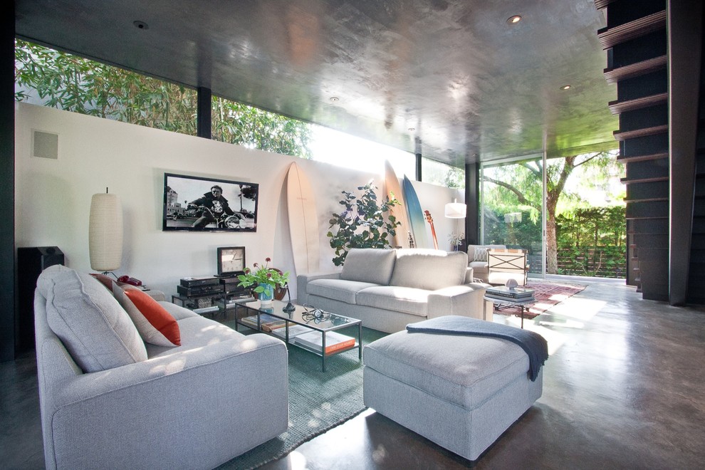 Cette image montre un salon design de taille moyenne et ouvert avec un mur blanc, sol en béton ciré, un téléviseur fixé au mur et un sol gris.