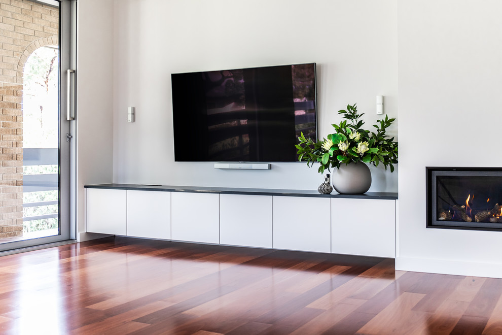 Mittelgroßes, Offenes Modernes Wohnzimmer mit weißer Wandfarbe, braunem Holzboden, Hängekamin, verputzter Kaminumrandung, TV-Wand und rotem Boden in Adelaide