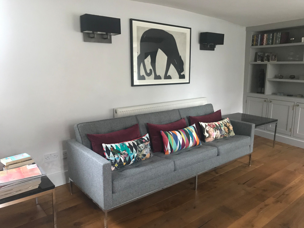 Photo of a medium sized contemporary formal living room in Oxfordshire with grey walls, medium hardwood flooring, a wood burning stove, a stone fireplace surround, a freestanding tv, brown floors, exposed beams and tongue and groove walls.