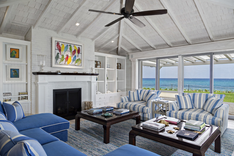 マイアミにある広いビーチスタイルのおしゃれなリビング (白い壁、標準型暖炉、レンガの暖炉まわり、テレビなし、青いソファ) の写真