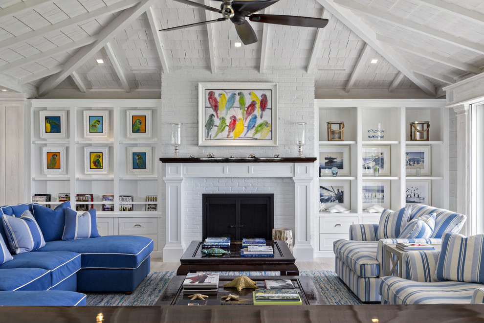 На фото: большая гостиная комната в морском стиле с белыми стенами, стандартным камином, фасадом камина из кирпича и синим диваном без телевизора