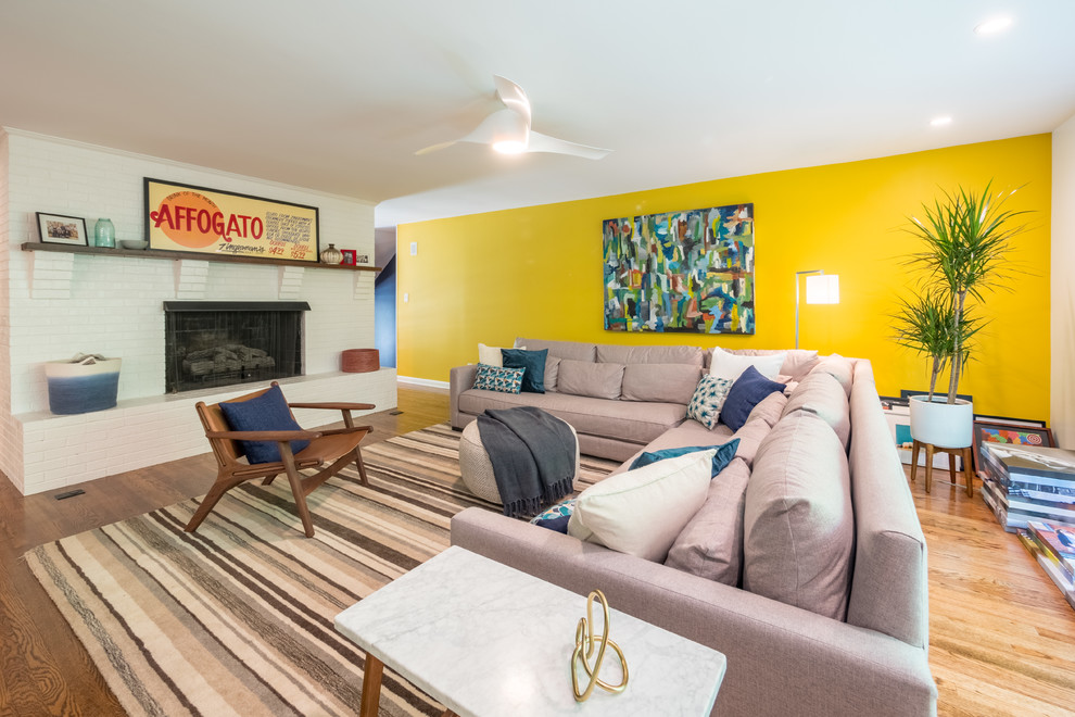 Foto di un soggiorno minimalista con pareti gialle, pavimento in legno massello medio, camino classico, cornice del camino in mattoni e pavimento marrone