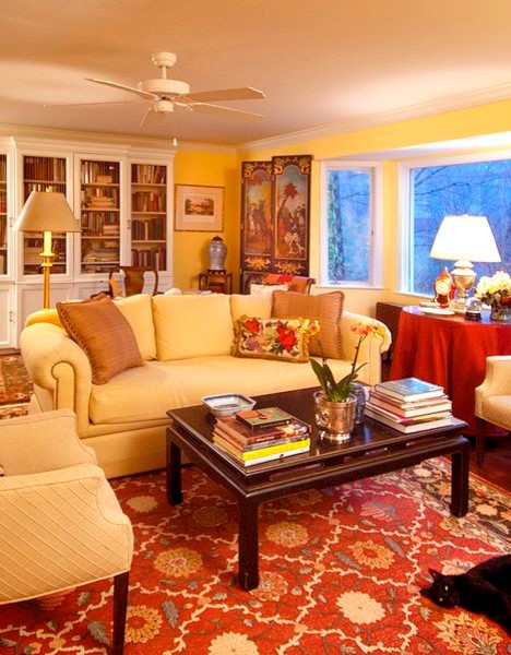 Eklektisk inredning av ett stort separat vardagsrum, med ett bibliotek, gula väggar, mörkt trägolv, en standard öppen spis, en spiselkrans i tegelsten och en inbyggd mediavägg