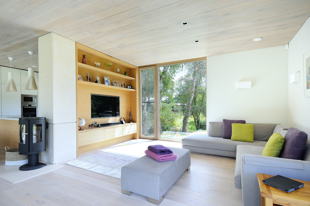 Cette image montre un salon design ouvert avec un mur blanc, parquet clair, un poêle à bois et un téléviseur encastré.