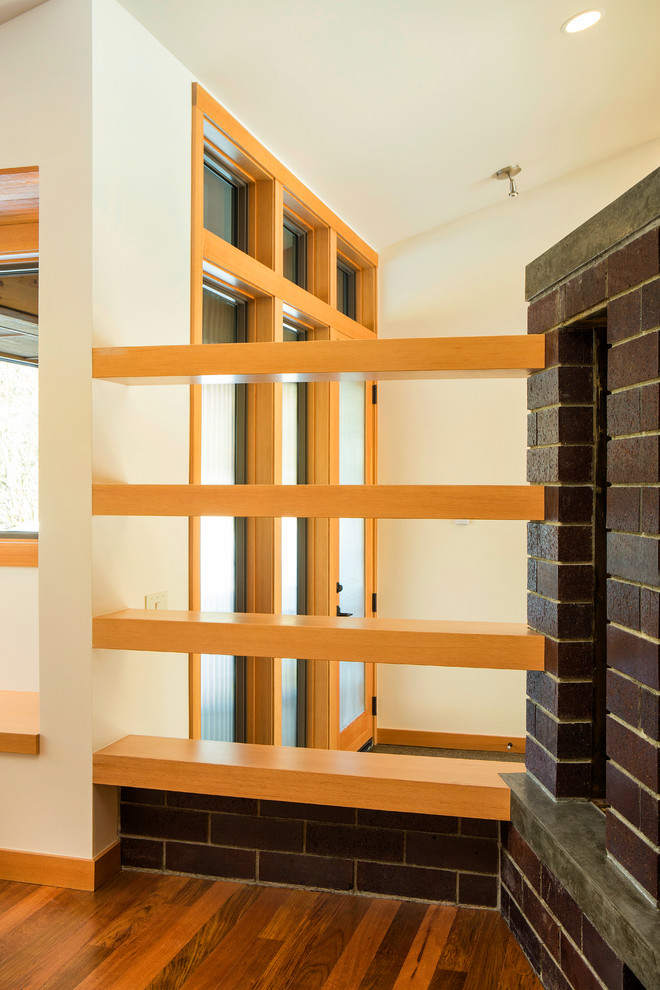 Cette image montre un salon design de taille moyenne et ouvert avec une cheminée double-face, un manteau de cheminée en brique, un mur beige et un sol en bois brun.
