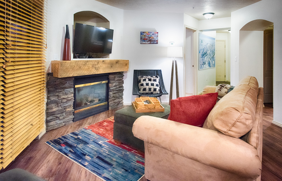 Foto på ett litet industriellt separat vardagsrum, med vita väggar, mörkt trägolv, en öppen hörnspis, en spiselkrans i sten och en väggmonterad TV