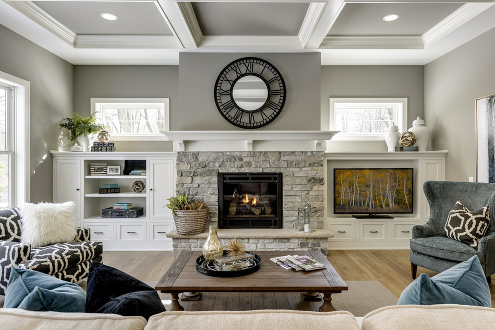 Inspiration pour un grand salon traditionnel ouvert avec un mur gris, parquet clair, une cheminée standard, un manteau de cheminée en pierre, un téléviseur encastré et un sol beige.