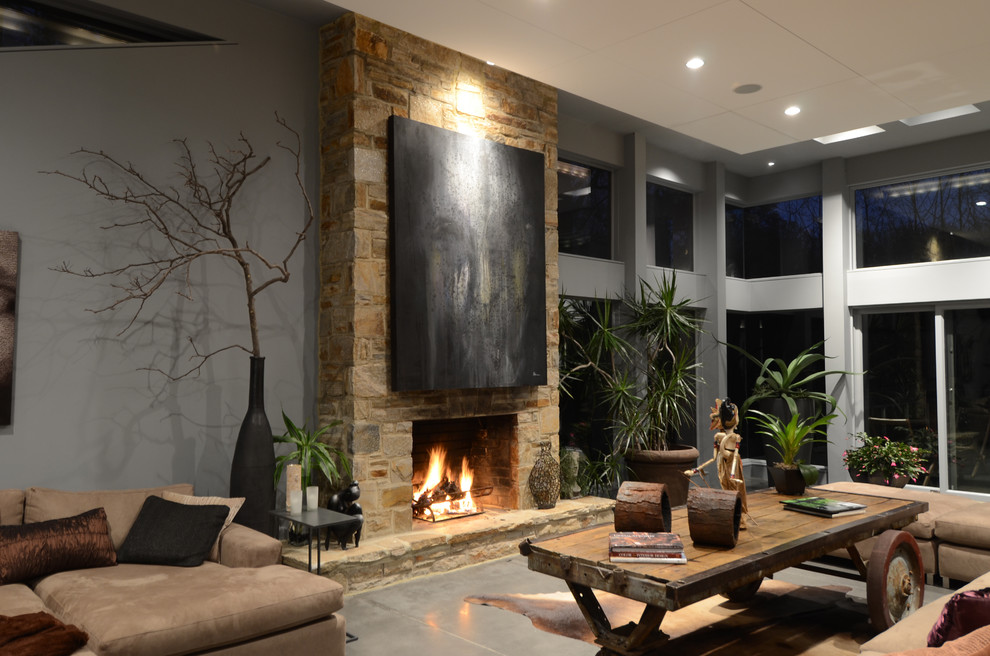 На фото: большая открытая гостиная комната в современном стиле с серыми стенами, бетонным полом, стандартным камином, фасадом камина из камня, серым полом и ковром на полу без телевизора с