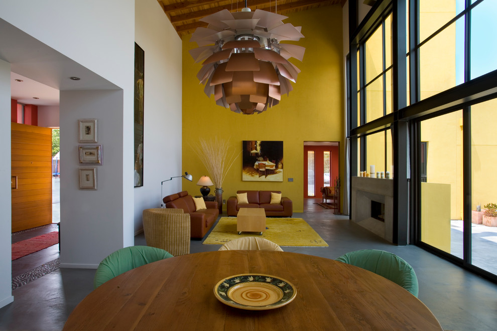 Imagen de salón abierto moderno grande con paredes amarillas, suelo de cemento, todas las chimeneas y marco de chimenea de hormigón