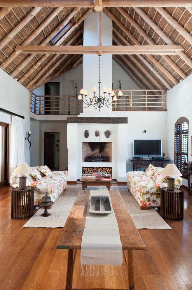 Country Wohnzimmer mit weißer Wandfarbe, braunem Holzboden, freistehendem TV und braunem Boden in Sonstige