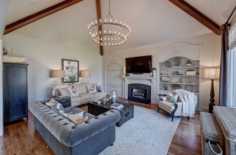 Inspiration for a large french country open concept medium tone wood floor, brown floor and exposed beam living room remodel in Charlotte with gray walls, a standard fireplace, a stone fireplace and a wall-mounted tv