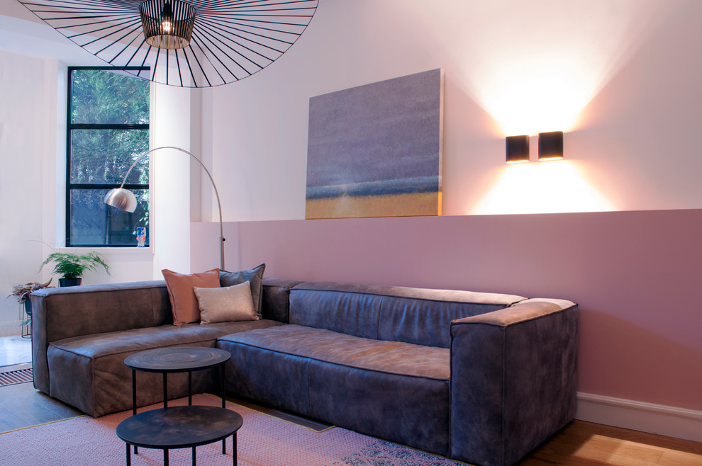 На фото: открытая гостиная комната среднего размера в стиле модернизм с розовыми стенами, светлым паркетным полом и телевизором на стене