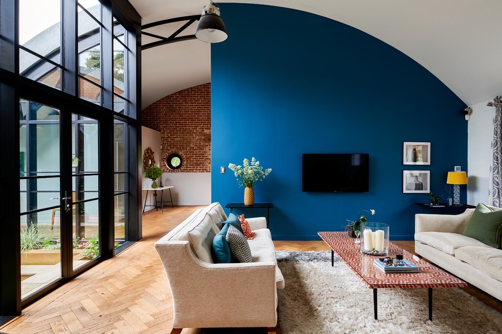 Cette image montre un très grand salon design ouvert avec un mur bleu, un sol marron, un sol en bois brun, aucune cheminée et un téléviseur fixé au mur.