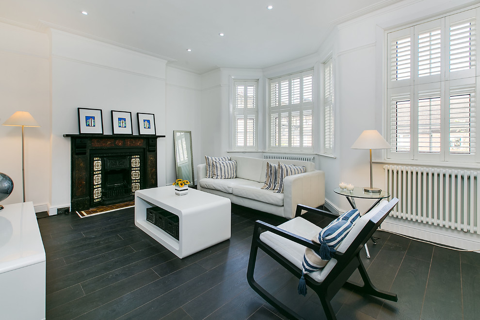 This is an example of a medium sized traditional formal living room in London with white walls, dark hardwood flooring and a standard fireplace.
