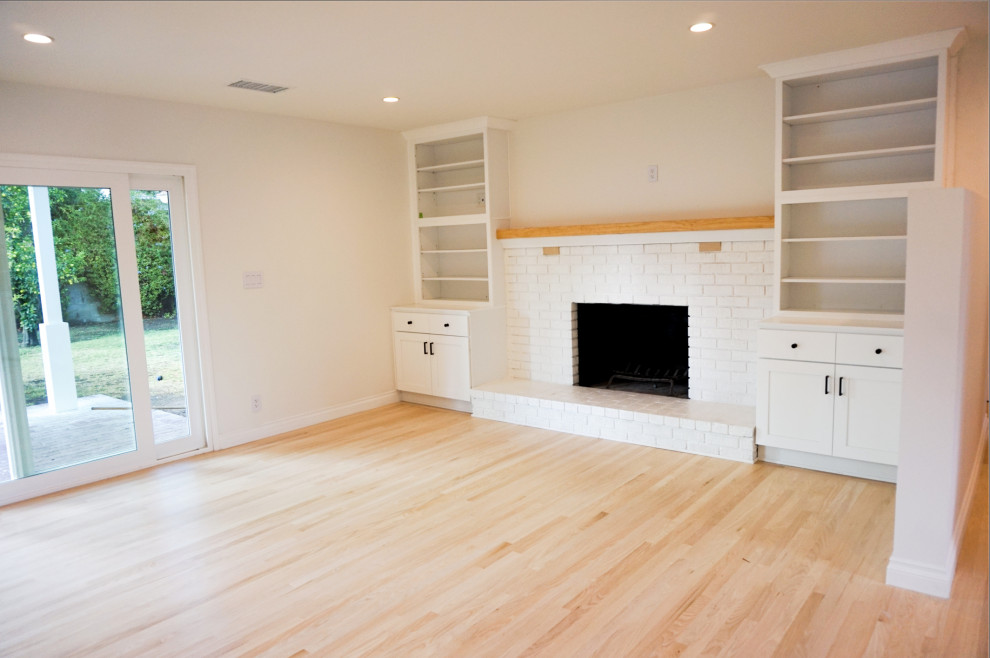 Cette image montre un salon minimaliste ouvert avec une salle de réception, un mur blanc, parquet clair, une cheminée standard, un manteau de cheminée en brique et un sol beige.