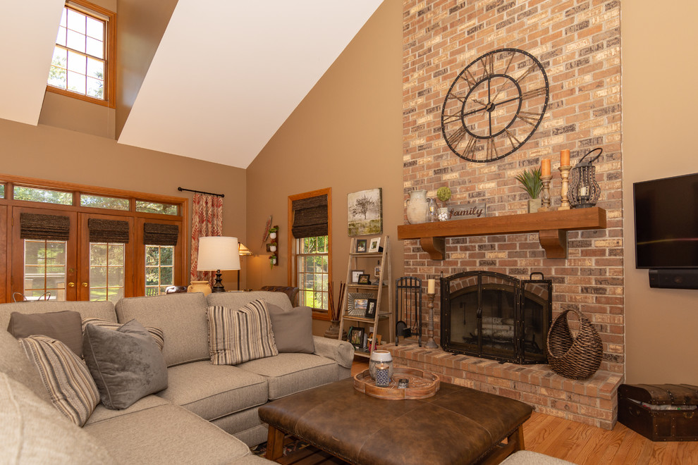 Large rustic formal enclosed living room in Chicago with beige walls, light hardwood flooring, a standard fireplace, a brick fireplace surround, a wall mounted tv and brown floors.