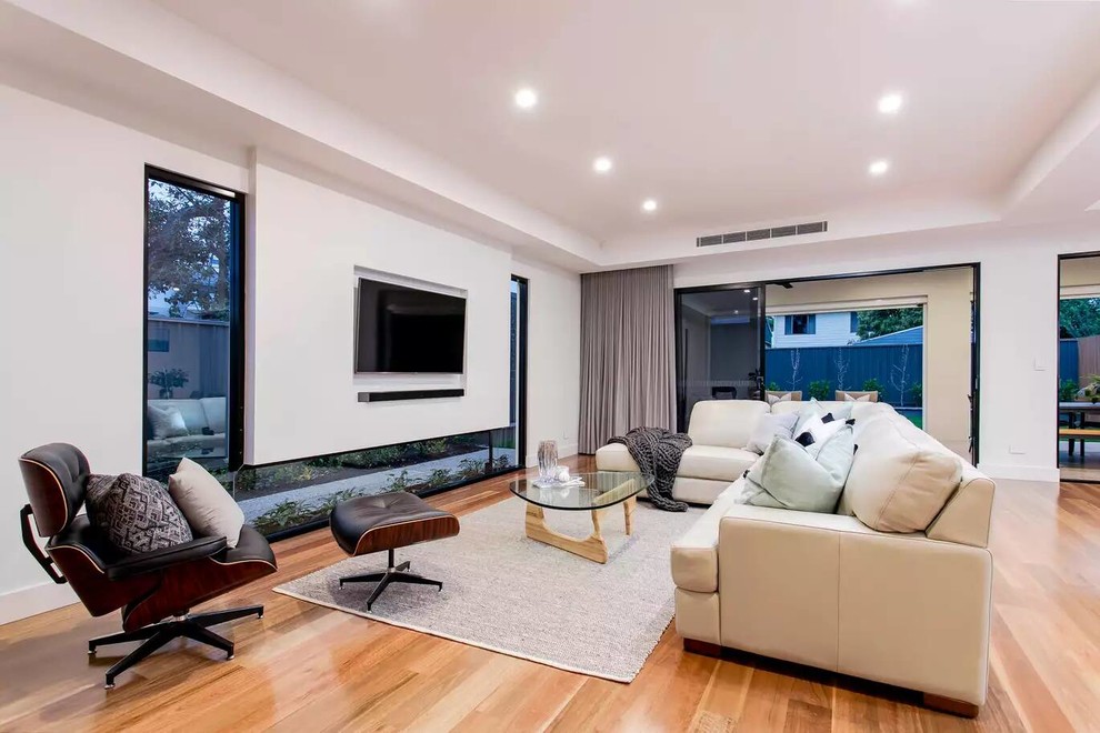 Пример оригинального дизайна: открытая гостиная комната в современном стиле с белыми стенами, паркетным полом среднего тона, телевизором на стене и коричневым полом