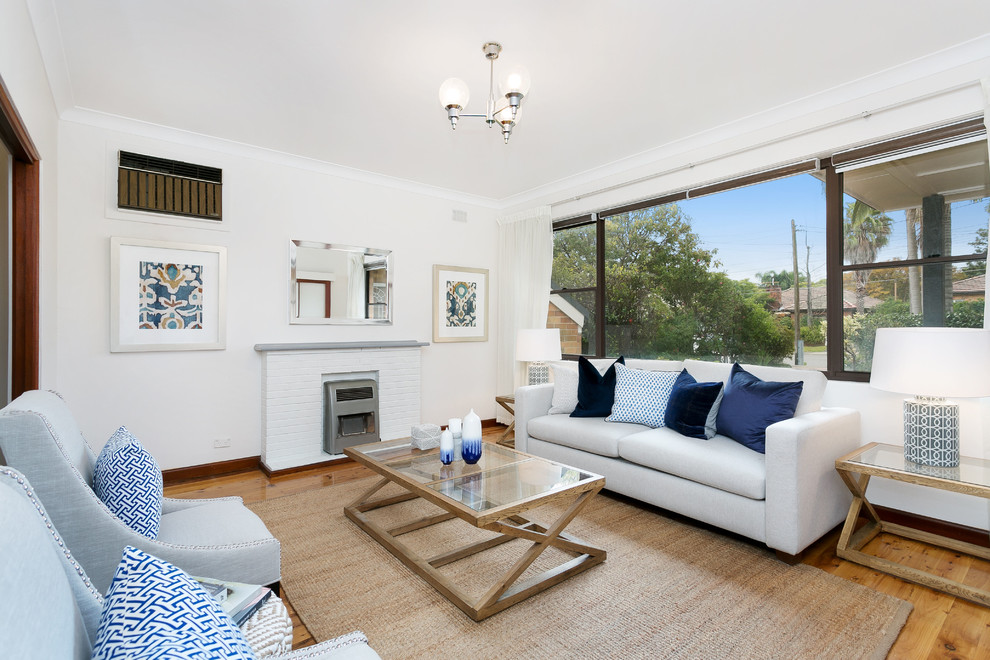 This is an example of a large contemporary open plan living room in Sydney with white walls, light hardwood flooring, a standard fireplace, a brick fireplace surround and a freestanding tv.
