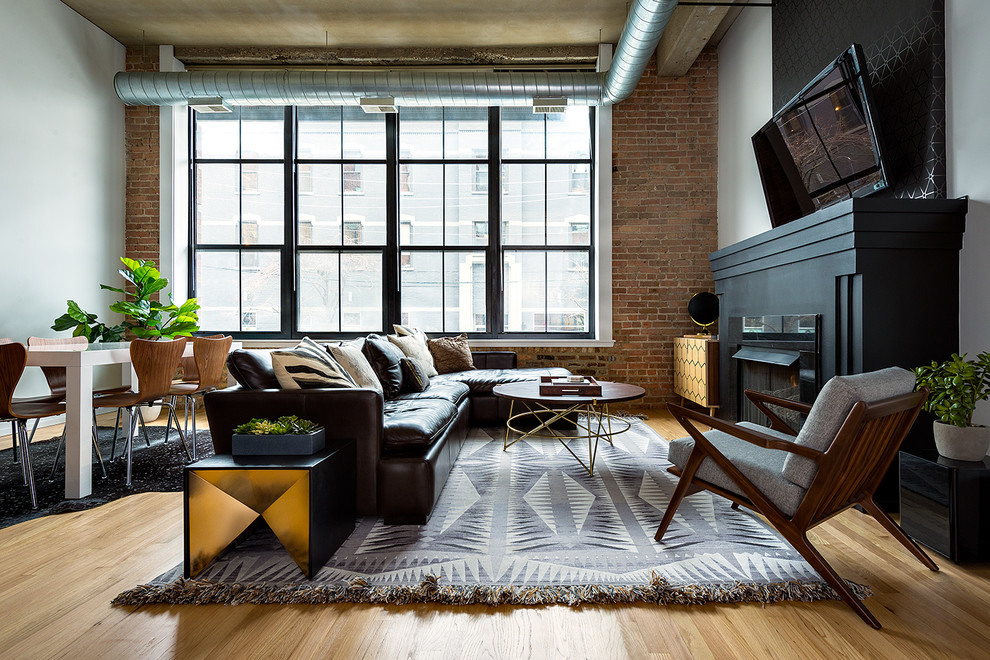 Imagen de salón abierto industrial con suelo de madera clara, todas las chimeneas, televisor colgado en la pared y alfombra