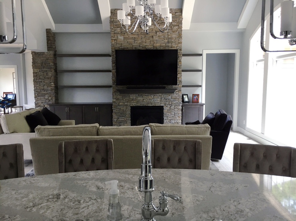 Стильный дизайн: большая открытая гостиная комната в стиле неоклассика (современная классика) с серыми стенами, светлым паркетным полом, стандартным камином, фасадом камина из камня, телевизором на стене и бежевым полом - последний тренд