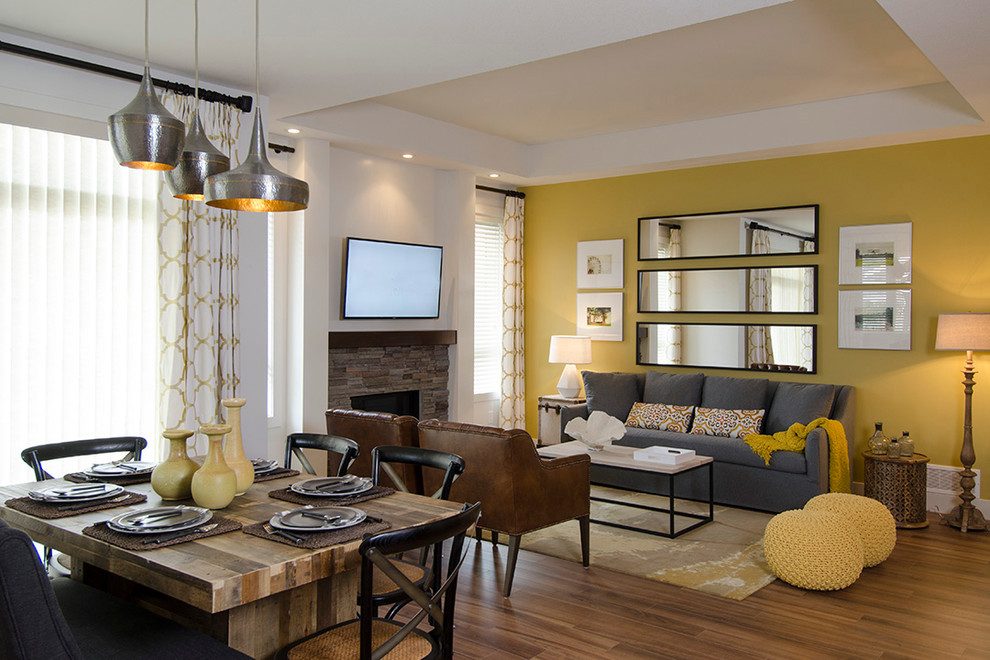 Modelo de salón para visitas abierto clásico renovado con paredes amarillas, suelo de madera oscura, marco de chimenea de piedra y televisor colgado en la pared