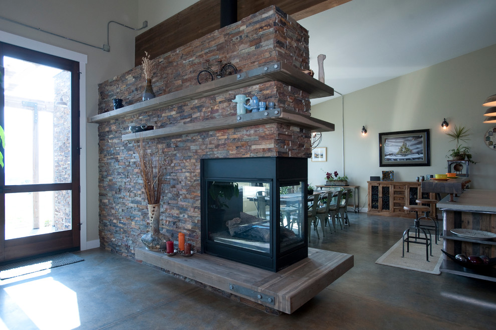 他の地域にある高級な広いインダストリアルスタイルのおしゃれなLDK (グレーの壁、コンクリートの床、両方向型暖炉、石材の暖炉まわり、テレビなし) の写真
