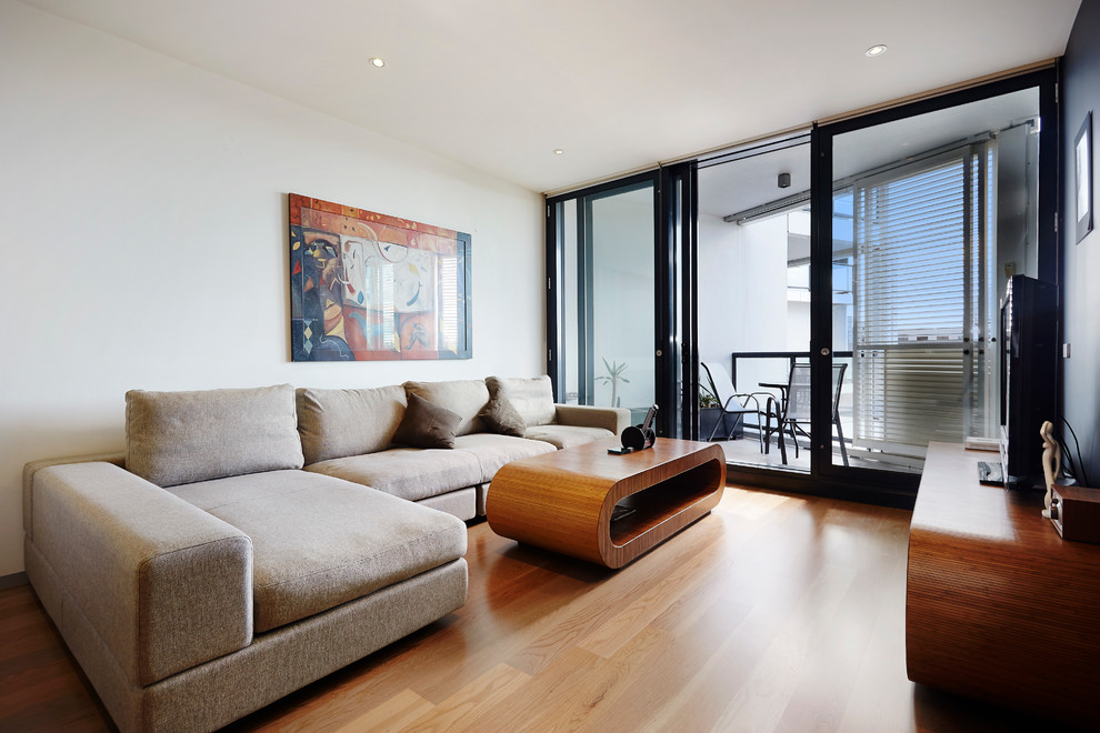 Пример оригинального дизайна: гостиная комната в современном стиле с белыми стенами, светлым паркетным полом и отдельно стоящим телевизором