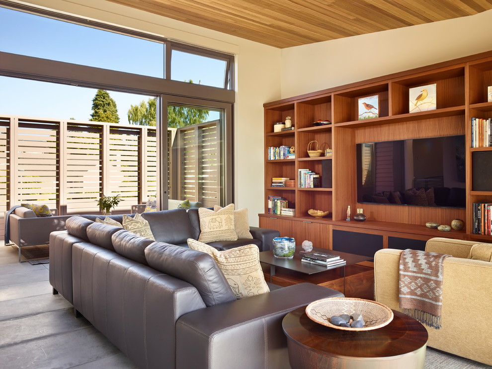 На фото: гостиная комната в современном стиле с бежевыми стенами, телевизором на стене и коричневым диваном