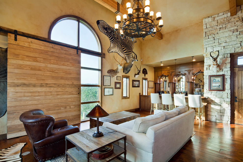 Diseño de salón con barra de bar abierto mediterráneo grande sin chimenea y televisor con paredes beige, suelo de madera oscura, suelo marrón y piedra