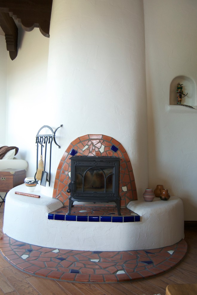 フェニックスにある小さな地中海スタイルのおしゃれなリビング (ベージュの壁、無垢フローリング、標準型暖炉、タイルの暖炉まわり、テレビなし、茶色い床) の写真