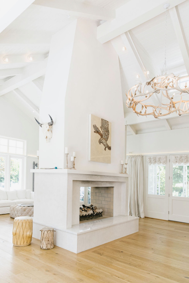 Example of a huge cottage formal and open concept light wood floor, brown floor and exposed beam living room design in Los Angeles with white walls, a two-sided fireplace, a concrete fireplace and no tv