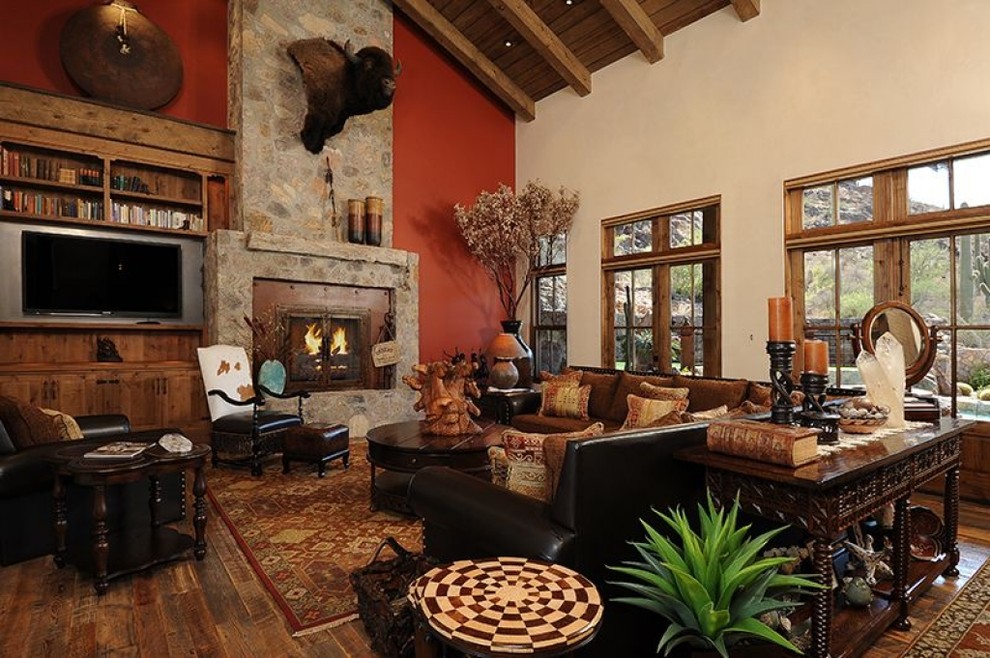 Cette photo montre un grand salon sud-ouest américain ouvert avec une salle de réception, un mur rouge, parquet foncé, une cheminée standard, un manteau de cheminée en pierre et un téléviseur fixé au mur.