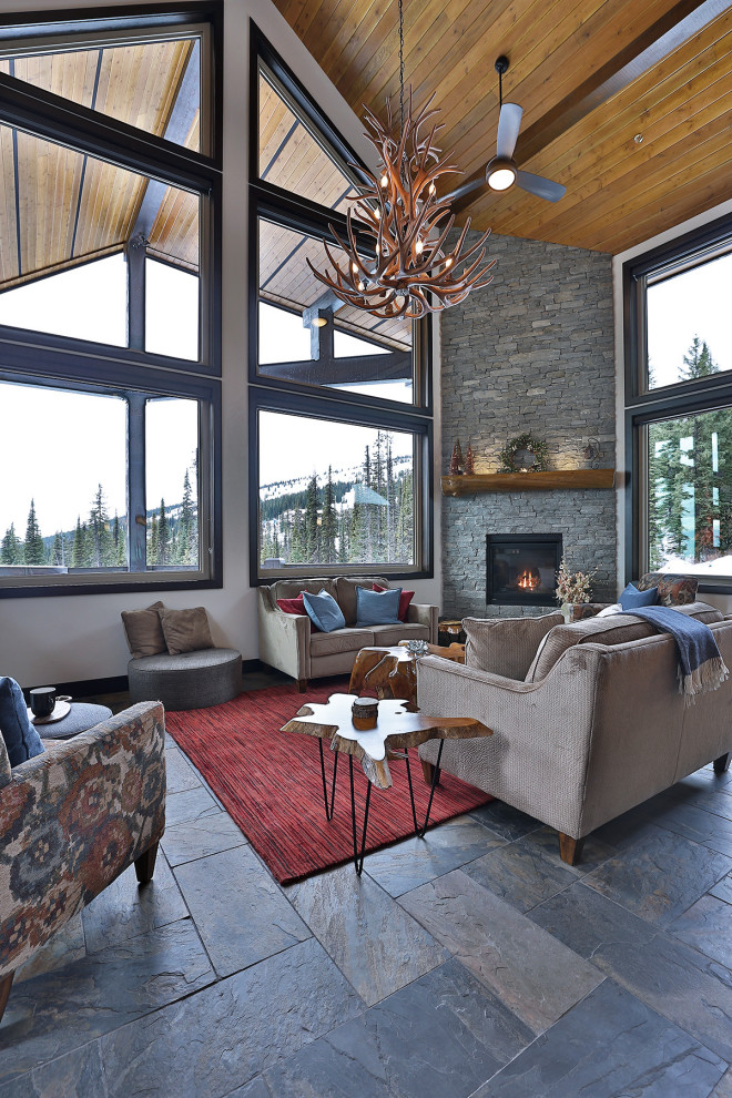 Example of a mountain style loft-style slate floor, gray floor and wood ceiling living room design in Vancouver with white walls, a corner fireplace, a stacked stone fireplace and a wall-mounted tv
