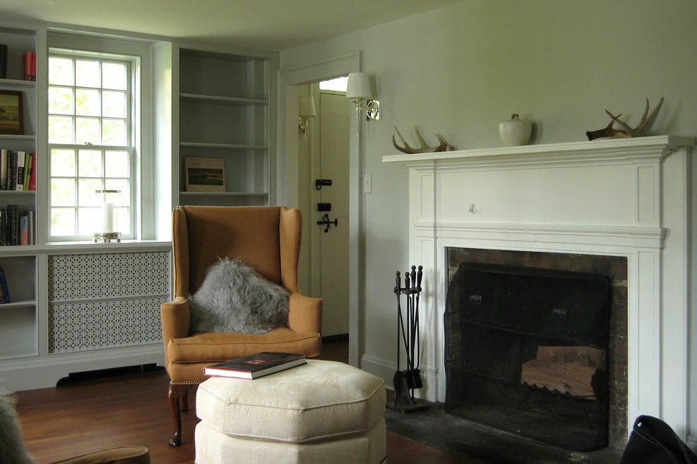 Cette photo montre un salon montagne de taille moyenne et fermé avec une bibliothèque ou un coin lecture, un mur gris, un sol en bois brun, une cheminée standard et aucun téléviseur.