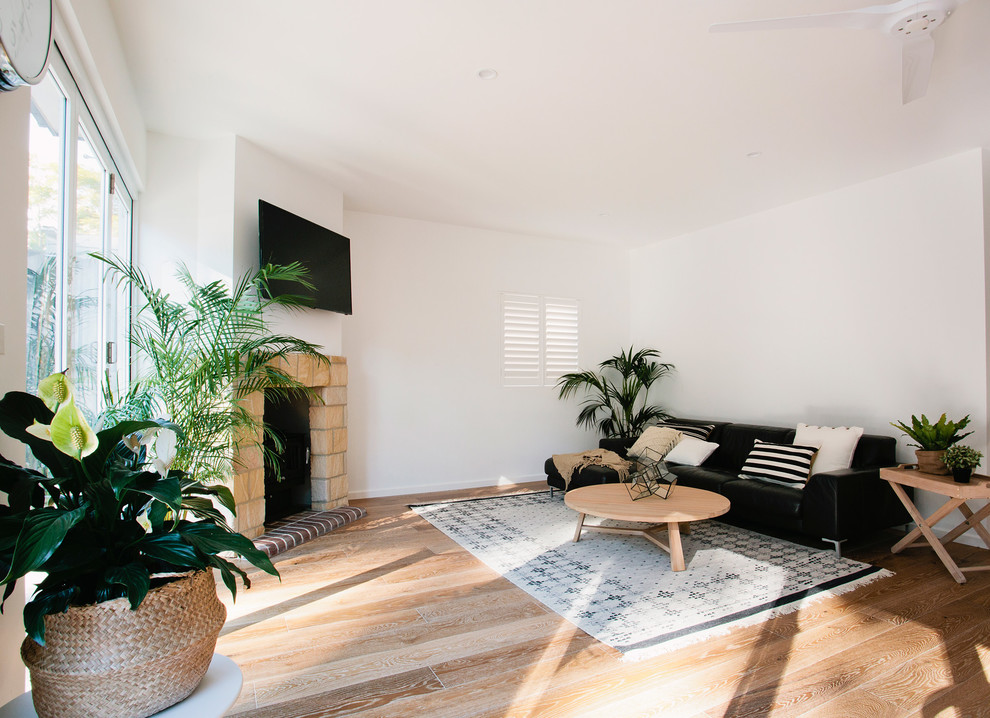 Example of a mid-sized beach style open concept medium tone wood floor living room design in Sydney with white walls, a standard fireplace, a stone fireplace and a wall-mounted tv