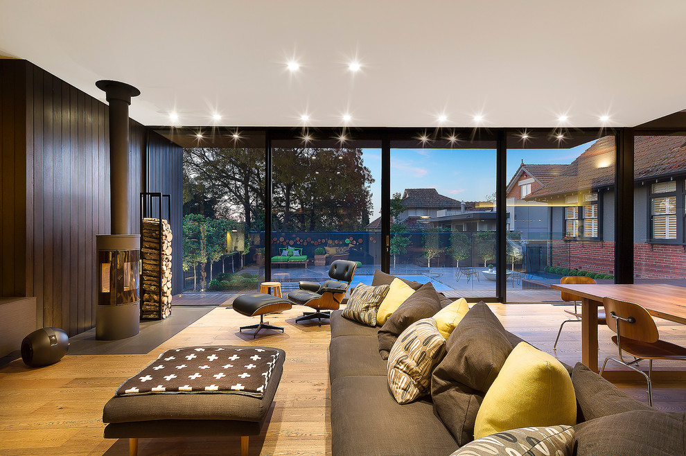 This is an example of a contemporary formal open plan living room in Melbourne with brown walls, medium hardwood flooring and a wood burning stove.