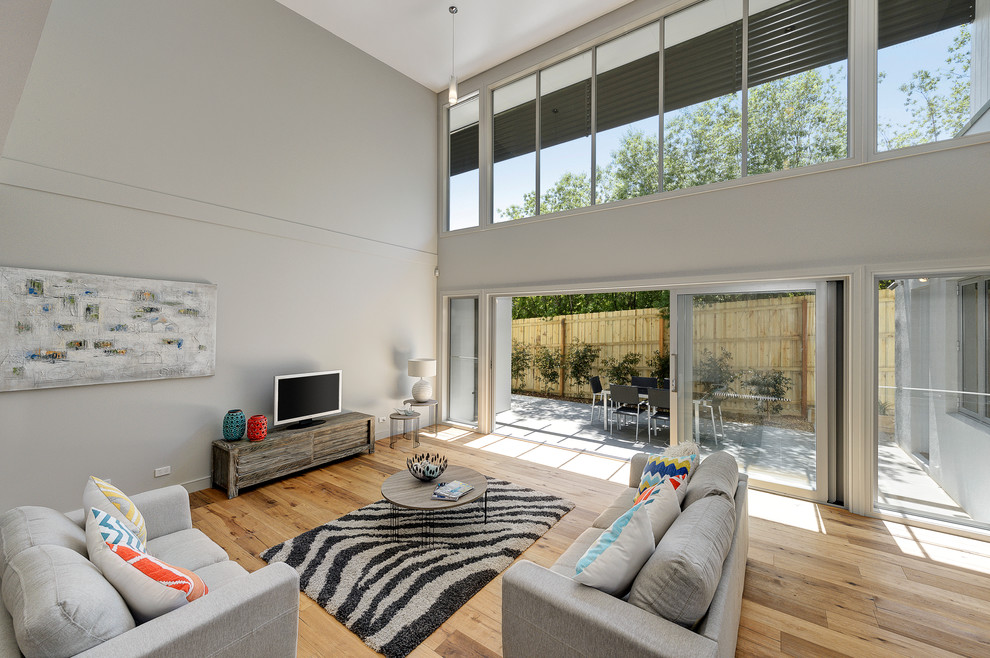 Großes, Offenes Modernes Wohnzimmer mit weißer Wandfarbe, braunem Holzboden und freistehendem TV in Melbourne