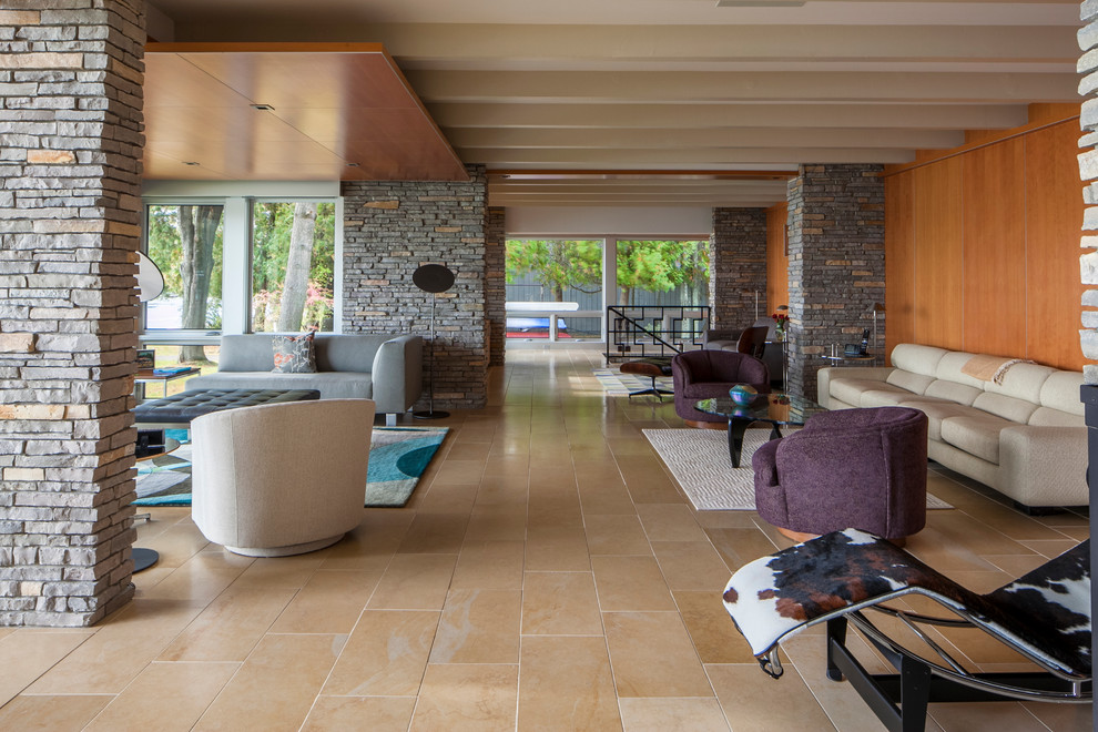 Идея дизайна: большая открытая гостиная комната в стиле ретро с полом из керамогранита, двусторонним камином, фасадом камина из камня и коричневыми стенами без телевизора