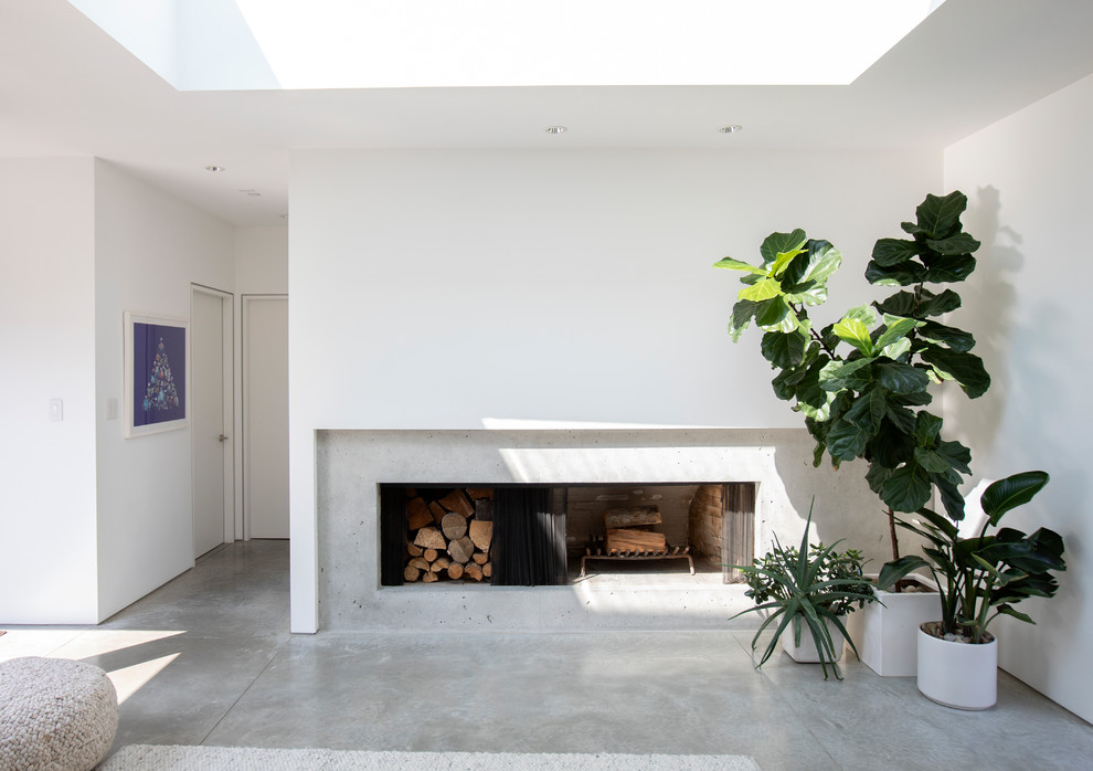 バンクーバーにある高級な中くらいなミッドセンチュリースタイルのおしゃれなリビング (白い壁、コンクリートの床、横長型暖炉、コンクリートの暖炉まわり、テレビなし、グレーの床) の写真