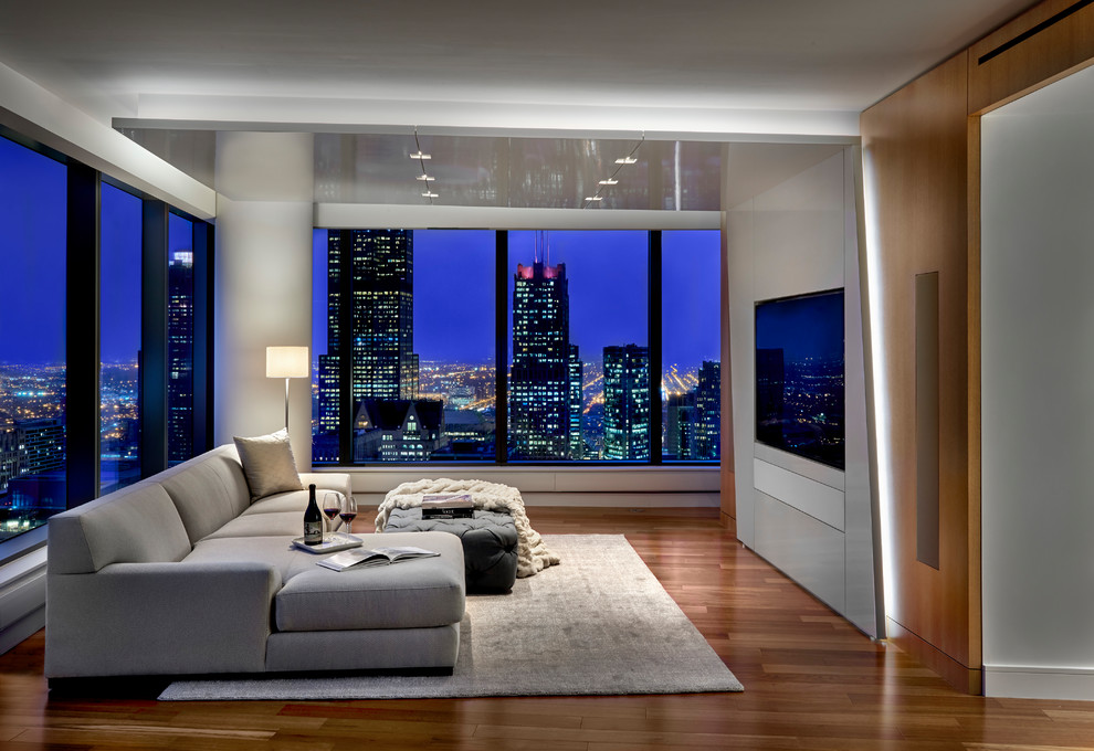 Стильный дизайн: гостиная комната в современном стиле с белыми стенами, паркетным полом среднего тона, телевизором на стене и коричневым полом - последний тренд