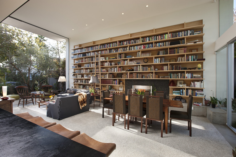 Ejemplo de biblioteca en casa abierta moderna pequeña con paredes blancas, suelo de cemento, todas las chimeneas y marco de chimenea de piedra